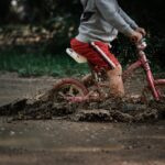child in gray jacket and red pants riding red bicycle on brown sand during daytime