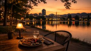 A quiet outdoor table at Zgara Korçare on the edge of Liqeni Artificial in Tirana at dusk, warm amber light, simple grilled meal